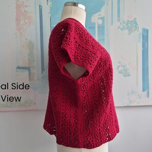 Puede incluir: Un top de ganchillo rojo con mangas cortas. La prenda se exhibe en un maniqu&iacute;, mostrando el intrincado dise&ntilde;o calado. El texto "Real Side View" es visible en el lado izquierdo de la imagen.