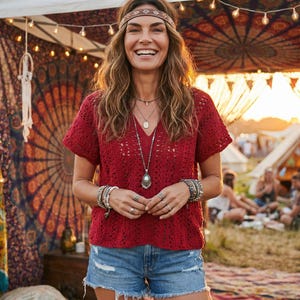 Puede incluir: Una mujer sonr&iacute;e, vistiendo un top de ganchillo rojo, pantalones cortos de mezclilla y una diadema marr&oacute;n. Lleva m&uacute;ltiples pulseras y collares. El fondo muestra una tienda decorada y personas.