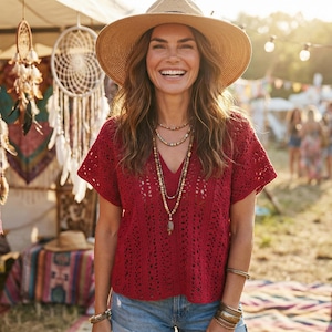 Puede incluir: Una mujer sonr&iacute;e, vistiendo un top de ganchillo rojo, pantalones cortos de mezclilla y un sombrero de paja. Lleva collares y pulseras superpuestos. El fondo muestra un mercado con atrapasue&ntilde;os y textiles coloridos, sugiriendo un tema bohemio.