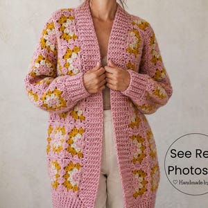 May include: A long, open-front cardigan in a granny square pattern. The sweater is primarily pink with yellow and cream-colored square accents. The sleeves are long, and the cardigan reaches to the mid-thigh. The text "See Real Photos" is visible.
