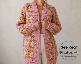 May include: A long, open-front cardigan in a granny square pattern. The sweater is primarily pink with yellow and cream-colored square accents. The sleeves are long, and the cardigan reaches to the mid-thigh. The text "See Real Photos" is visible.