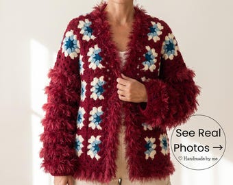 May include: A burgundy crochet cardigan with a floral pattern in white and blue. The cardigan has a fluffy trim around the collar and sleeves. The text "See Real Photos" is in a circle.