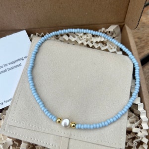Peut inclure: Un bracelet en perles bleu clair avec une seule perle blanche et deux perles dorées.