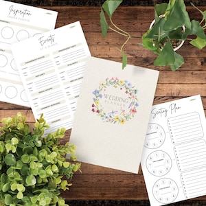 May include: A wedding planner with a floral wreath design and the text "Wedding Planner". The planner includes sections for events at a glance, seating plan, and inspiration.