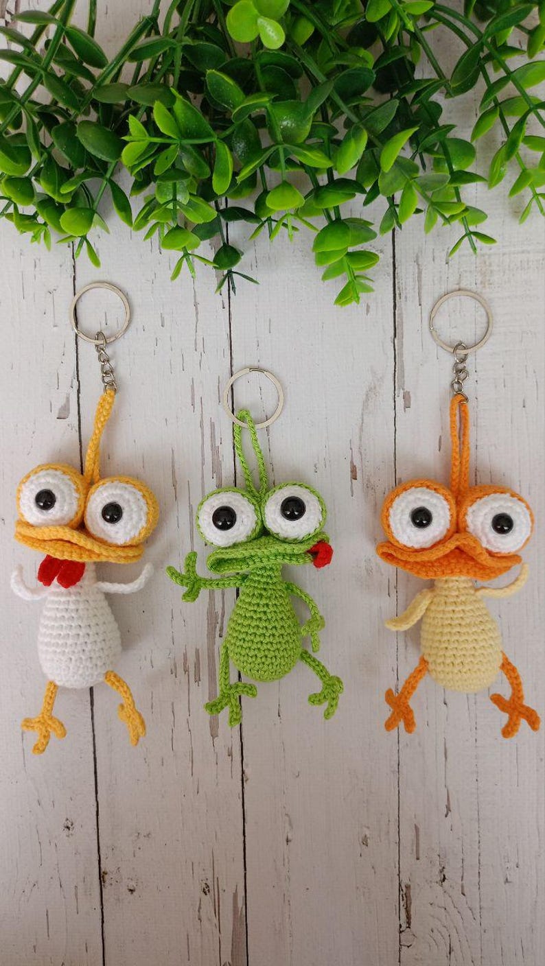 May include: Three handmade crochet keychains featuring whimsical cartoon characters. One is white with a red accent, another is green, and the third is orange. Each has large, googly eyes and a metal keyring.