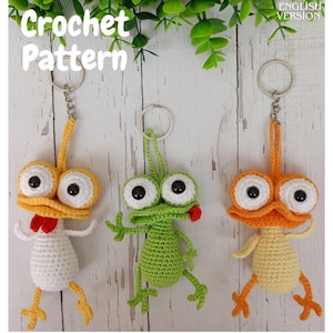 Puede incluir: Tres llaveros de ganchillo hechos a mano con forma de personajes de dibujos animados. Uno es blanco con detalles amarillos y rojos, otro es verde y el tercero es naranja y amarillo. Los llaveros tienen ojos grandes y saltones y están unidos a llaveros plateados. El texto "Crochet Pattern" es visible.