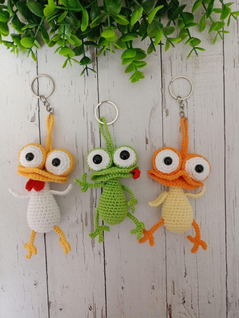 May include: Three handmade crochet keychains. One is a white chicken with yellow feet and a red comb. The second is a green frog with a red tongue. The third is an orange duck with yellow feet. All have large googly eyes.