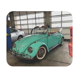 Pode incluir: Um Volkswagen Beetle conversível azul turquesa com o teto rebaixado, estacionado em uma garagem. O carro tem pneus de banda branca e um para-choque cromado.