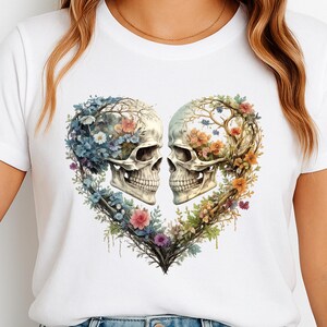 Könnte beinhalten: Weißes T-Shirt mit einem herzförmigen Design aus zwei Totenköpfen. Die Totenköpfe sind mit Blumen und Ranken in Blau-, Rosa-, Orange- und Grüntönen verziert. Das Design ist mittig auf dem T-Shirt platziert.