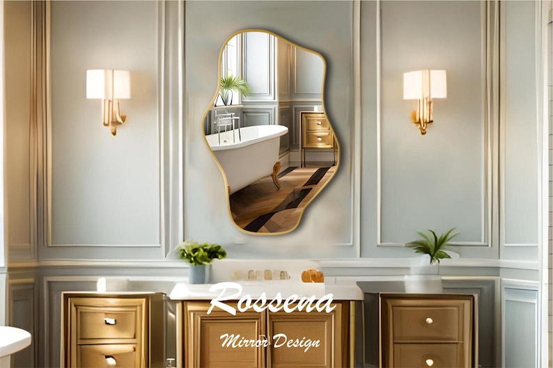 Puede incluir: Un espejo de forma irregular con marco dorado, que refleja una ba&ntilde;era blanca y un armario dorado. El espejo est&aacute; colgado en una pared blanca con molduras doradas. El texto "Rosseena Mirror Design" est&aacute; impreso debajo del espejo.