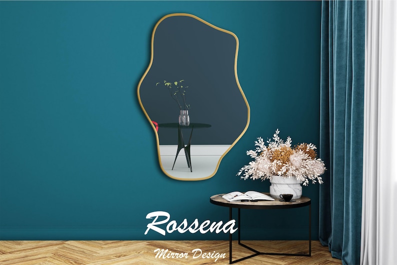 Puede incluir: Un espejo de forma abstracta con marco dorado y superficie de vidrio azul oscuro. El espejo est&aacute; colgado en una pared azul turquesa con una mesa peque&ntilde;a y un jarr&oacute;n de flores delante. El texto "Rossena Mirror Design" est&aacute; debajo del espejo.
