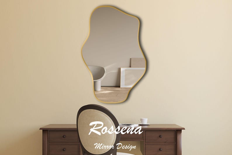 Puede incluir: Un espejo de forma irregular con marco dorado, que refleja una habitaci&oacute;n con una silla blanca y un escritorio de madera. El espejo est&aacute; colgado en una pared beige. El texto "Rosseena Mirror Design" est&aacute; debajo del espejo.