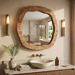 Peut inclure: Une scène de salle de bain avec un grand miroir en bois de forme irrégulière. Le miroir reflète une salle de bain lumineuse avec une baignoire et une douche. En dessous, un lavabo ovale blanc, des robinets en laiton et un meuble en bois. Deux appliques en laiton encadrent le miroir.