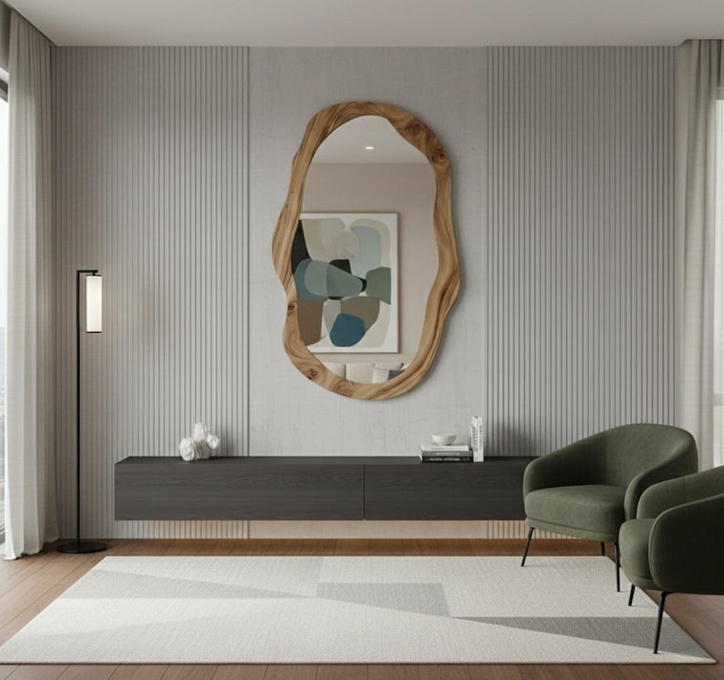 May include: A modern living room featuring a large, organically shaped wooden mirror. Below the mirror is a dark gray cabinet, with two green armchairs and a geometric patterned rug. A black floor lamp stands to the left.