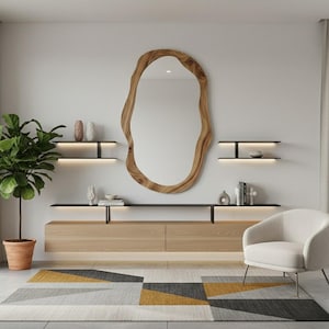 May include: A modern living room featuring a large, organic-shaped wooden mirror. Below the mirror is a light wood cabinet with black shelves and decorative items. A patterned rug in gray, yellow, and black sits on the floor, with a white armchair and potted plant.