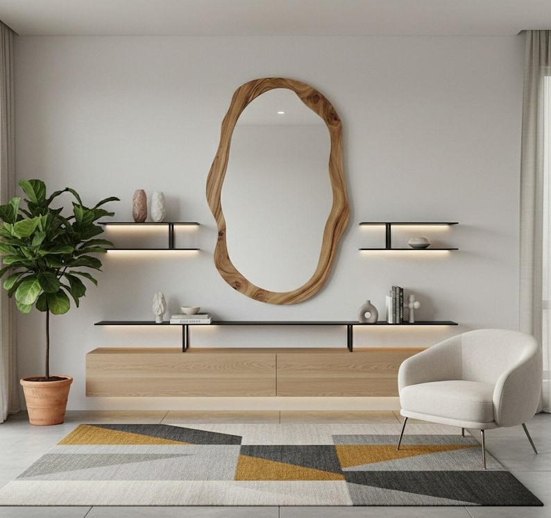 May include: A modern living room featuring a large, organic-shaped wooden mirror. Below the mirror is a light wood cabinet with black shelves and decorative items. A patterned rug in gray, yellow, and black sits on the floor, with a white armchair and potted plant.