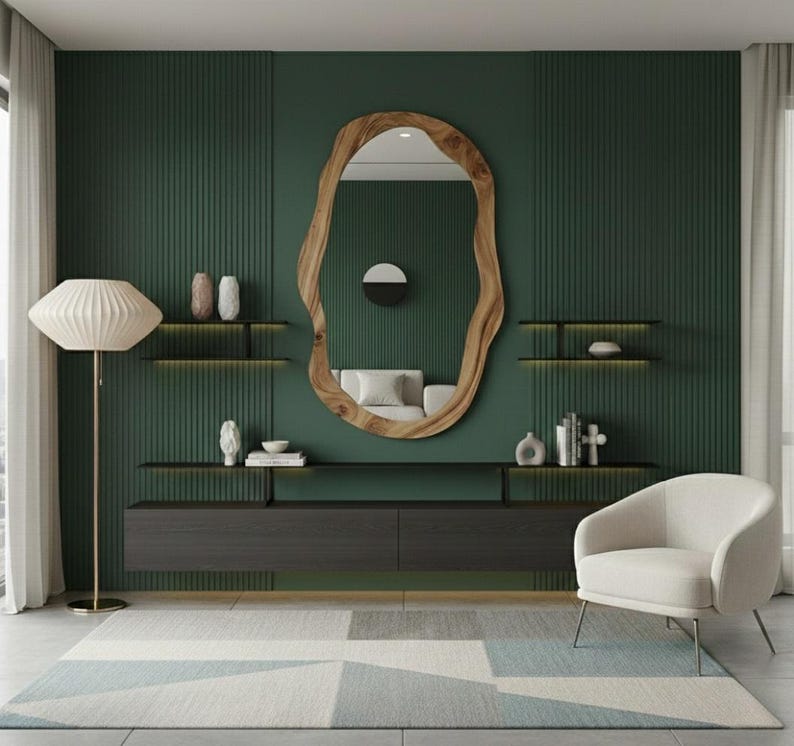 May include: A modern living room with a dark green accent wall, featuring a large, organic-shaped wooden mirror. The room includes a white armchair, a floor lamp, floating shelves, and a low cabinet. A geometric rug adds a touch of color.