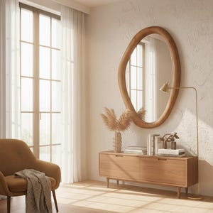 May include: A modern living room with a large, irregularly shaped wooden mirror. A wooden cabinet with books and decorative items sits below the mirror. A gold floor lamp and an upholstered chair with a blanket complete the scene.