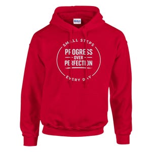 Puede incluir: Una sudadera con capucha roja con texto blanco. El texto dice "SMALL STEPS - PROGRESS OVER PERFECTION - EVERY DAY" en un diseño circular. La sudadera tiene un bolsillo delantero y una capucha con cordón.