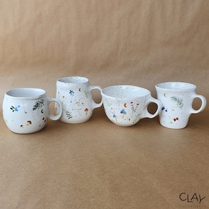 Puede incluir: Cuatro tazas de cerámica blanca con esmalte moteado y diseños florales y de hongos pintados a mano. Las tazas tienen diferentes formas y tamaños.