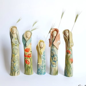 Puede incluir: Cinco figuritas de cerámica de mujeres con diseños florales y un solo tallo de trigo que se extiende desde la parte superior de cada figura.