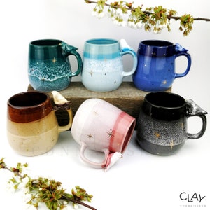 May include: Six ceramic mugs with a bird figurine on the handle. The mugs are in different colors and have a speckled glaze. The mugs are arranged in a row on a wooden surface.