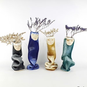 May include: Four ceramic vases with painted faces and dried flowers. The vases are in shades of blue, green, black, and gold.