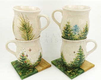 May include: Four ceramic mugs with a winter forest design. The mugs are stacked in pairs and are sitting on green and wood coasters. The mugs are white with green, blue, and gold accents.