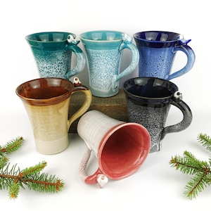 May include: Six ceramic mugs with bird-shaped handles. The mugs are in various colors, including teal, blue, brown, black, white, and pink. The mugs are all glazed and have a speckled finish.