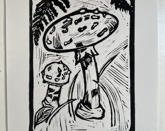 May include: Black and white linocut print of two mushrooms. The larger mushroom has a rounded cap with dark spots. The smaller mushroom is to the left, with a similar cap design. Ferns and grass are in the background.