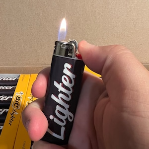 May include: A black Bic lighter with the word "lighter" printed in white with red outlines. The lighter is lit and the flame is visible.