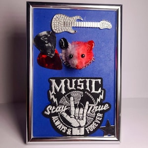 May include: Framed artwork with a blue background, featuring a rhinestone-studded guitar, a red and gray hamster, and a patch with the words "MUSIC Stay True Always & Forever" and a hand gesture. Includes guitar picks and a star.