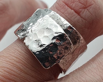 May include: A silver ring with a hammered texture. The ring is wide and has a unique, asymmetrical design.