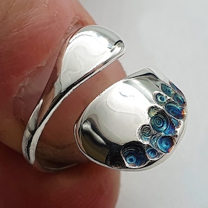 Puede incluir: Un anillo de plata con un diseño único que presenta un patrón de espiral y acentos azules.