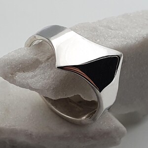 May include: A silver ring with a unique, geometric design. The ring is made of polished metal and has a sharp, angular shape.