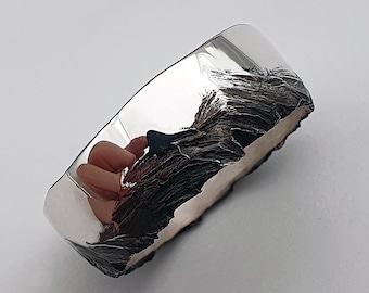 May include: A silver ring with a textured, organic design. The ring is polished on one side and has a rough, textured finish on the other side.
