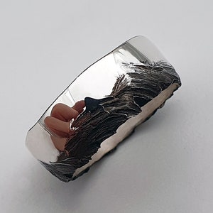 May include: A silver ring with a textured, organic design. The ring is polished on one side and has a rough, textured finish on the other side.