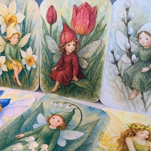 Op de afbeelding: Een verzameling aquarelkaarten met feeën in een tuin. De kaarten tonen feeën met vleugels, gekleed in verschillende kleuren, omringd door bloemen zoals narcissen, tulpen en sneeuwklokjes. Het kunstwerk heeft een zachte, grillige stijl.