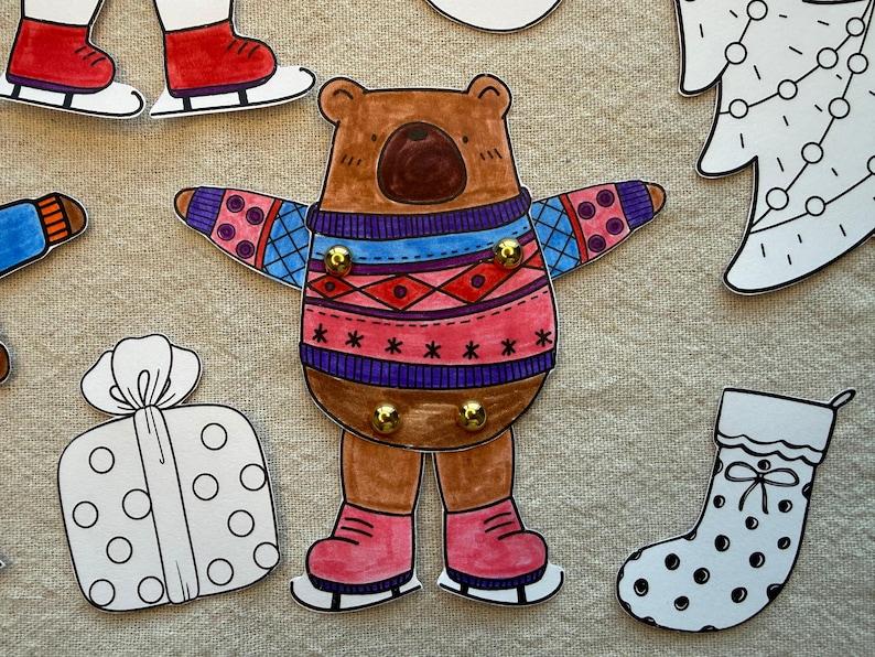Puede incluir: Ilustraci&oacute;n de un oso pardo con un su&eacute;ter colorido y patines. El oso tiene una nariz marr&oacute;n oscuro y est&aacute; rodeado de otros recortes tem&aacute;ticos navide&ntilde;os, incluyendo un regalo, un calcet&iacute;n y un &aacute;rbol de Navidad.