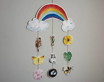 May include: A colorful rainbow mobile with hanging decorations including a butterfly, a bird, a flower, a bunny, a leaf, a nest with eggs, and a bee.