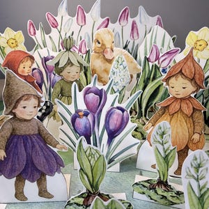 Pode incluir: Um diorama de papel caprichoso com figuras ilustradas de crianças em trajes de flores, um patinho e várias flores da primavera. A cena é preenchida com flores roxas, amarelas e brancas, criando uma estética de conto de fadas encantadora.