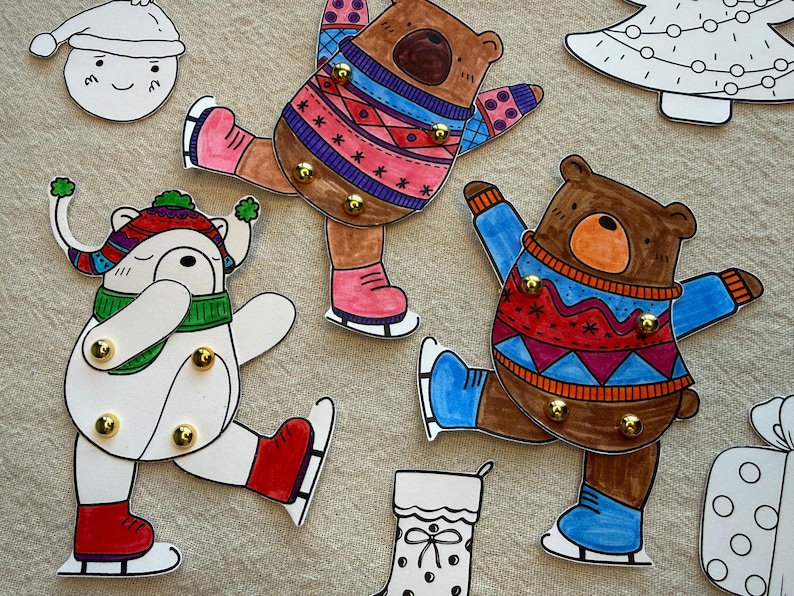 Puede incluir: Recortes de papel navide&ntilde;os dibujados a mano de osos y un oso polar patinando sobre hielo, con su&eacute;teres y sombreros. Otros recortes incluyen un mu&ntilde;eco de nieve, un &aacute;rbol de Navidad, un calcet&iacute;n y una caja de regalo.