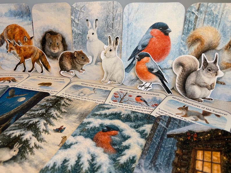 May include: A selection of winter-themed paper cutouts, including a fox, squirrel, and birds, arranged on illustrated cards. The cards depict winter scenes and text. The colour scheme features white, brown, and red.
