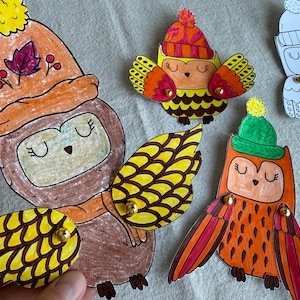 Può includere: Ritagli di gufo disegnati a mano con gli occhi chiusi, che indossano cappelli e sciarpe colorati. I gufi hanno ali gialle, arancioni, marroni e rosse. Alcuni hanno borchie dorate come accenti. I gufi sono un artigianato stravagante a tema autunnale.
