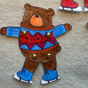 Puede incluir: Ilustraci&oacute;n de un oso pardo con un su&eacute;ter azul y rojo y patines azules. El oso tiene una nariz naranja y est&aacute; decorado con tachuelas doradas. En el fondo se ven patines y un calcet&iacute;n adicionales.