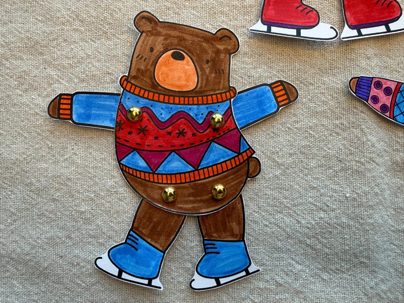 Puede incluir: Ilustraci&oacute;n de un oso pardo con un su&eacute;ter azul y rojo y patines azules. El oso tiene una nariz naranja y est&aacute; decorado con tachuelas doradas. En el fondo se ven patines y un calcet&iacute;n adicionales.