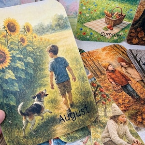 May include: A collection of seasonal art cards. One card features a boy and a dog in a field of sunflowers, labeled "August." Other cards depict scenes of summer, autumn, and winter. The cards have a watercolor style and are suitable for home decor or as gifts.
