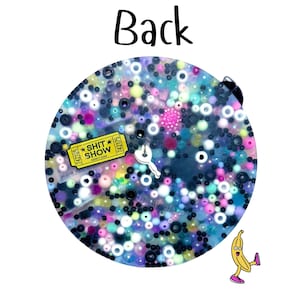 Puede incluir: Un llavero redondo y brillante con una mezcla de cuentas coloridas y un dije amarillo en forma de boleto que dice "SHIT SHOW". Tambi&eacute;n se ve un peque&ntilde;o dije blanco en forma de llave y un pl&aacute;tano de dibujos animados.