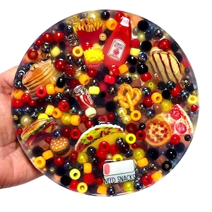 May include: A round resin coaster filled with miniature food items like fries, a burger, pizza, and a taco. The coaster also includes beads in red, yellow, and black, with the text "NEED SNACKS".