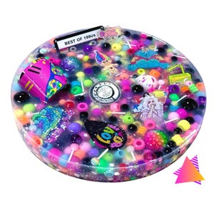May include: A clear, round resin art piece filled with colorful beads, lollipops, and various 1980s-themed charms. The piece includes a miniature telephone, a cassette player, and a charm that says "BEST OF 1980s".